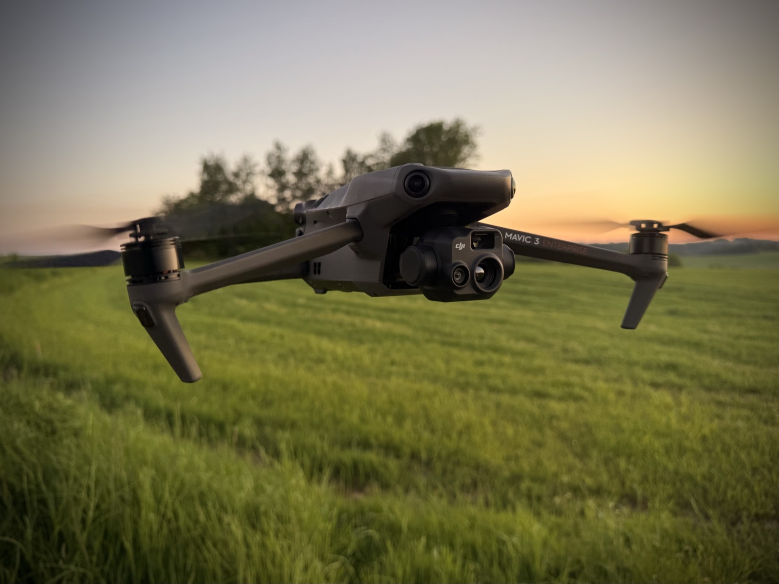 DJI Mavic 3T Enterprise im Flug ueber einer Wiese, Doppelkamera (RGB plus W&auml;rmebild) an der Front-Gimbal.
